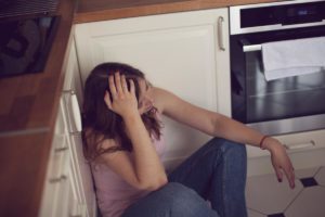 distraught young woman sitting on kitchen floor with head in her hands wondering what is an eating disorder