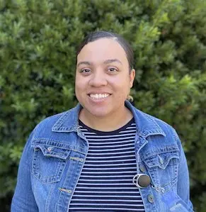 Woman with short dark hair wearing denim jacket and striped shirt smiling at camera