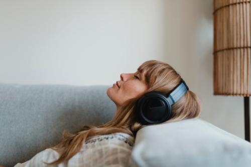 woman relaxing on her couch while listening to podcasts and music on her headphones