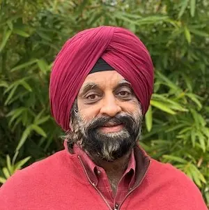 Man wearing a red shirt and pink turban, smiling at camera against a green leafy background