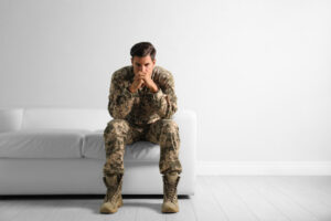 stressed military man in uniform sitting on sofa near white wall indoors.