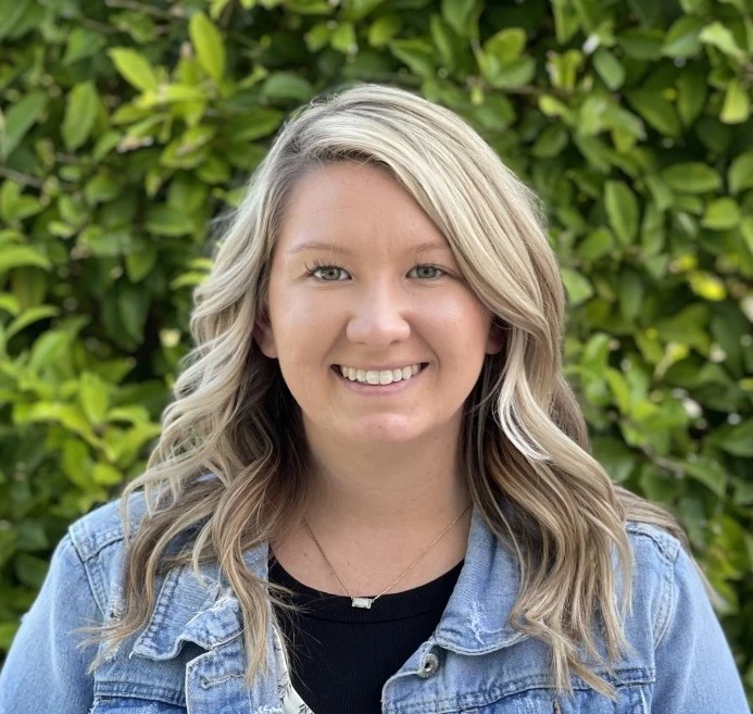 Woman with blonde wavy hair wearing denim jacket and black top smiling