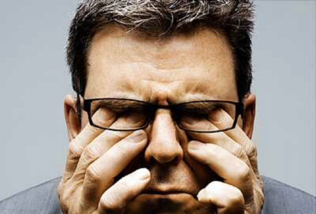 close up of man rubbing his tired eyes behind his glasses