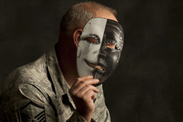 older man obscuring face by holding up a comedy-tragedy mask