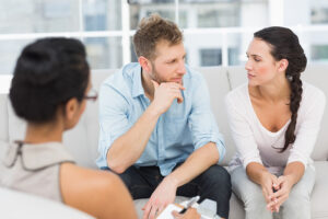 man and woman sitting on couch looking at each other while female therapist watches