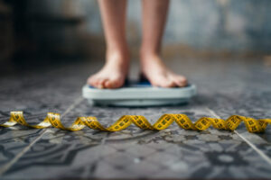 feet and lower legs of person standing on scale while a measuring tape is in the foreground