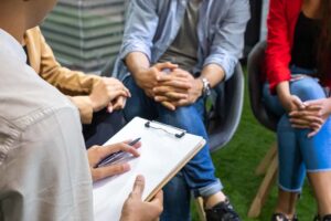 therapist with clipboard leading small group of adults outdoors