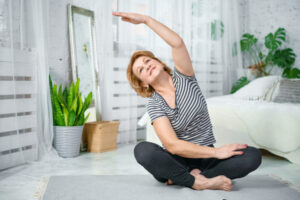 older woman exercising in floor of her bedroom by stretching on a yoga mat