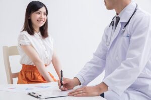doctor talking to young female patient as he writes notes on clipboard
