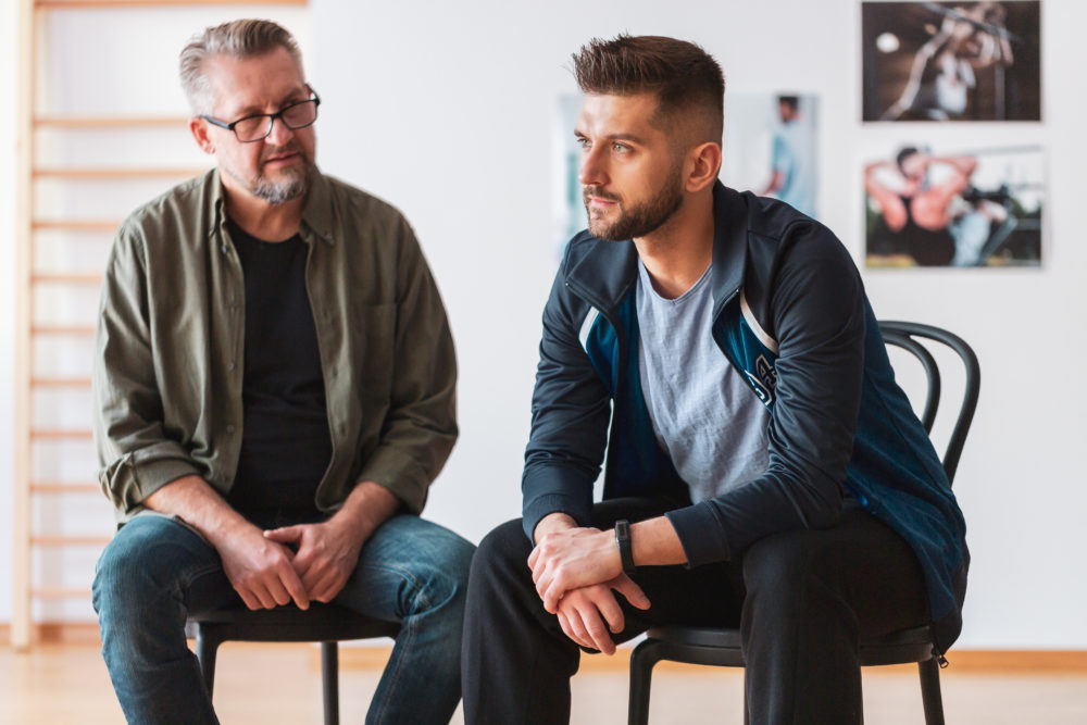 older man sitting next to younger man offering support in therapy session