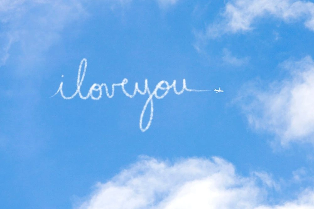 Handwritten text 'i love you' written across blue sky with white clouds