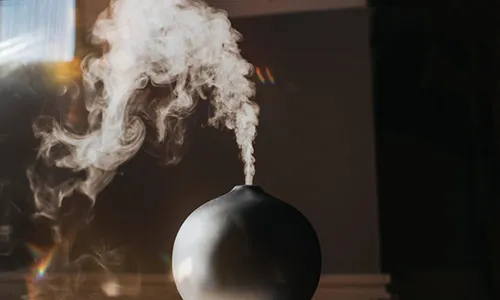Close-up photograph of steam rising from a black spherical diffuser with warm lighting in the background