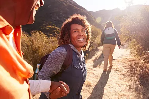 Group of hikers on a mountain trail, with a smiling woman in center wearing backpack turning toward camera
