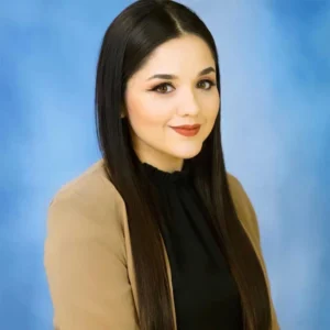 Woman with long dark hair wearing beige cardigan over black top, smiling at camera against blue background.