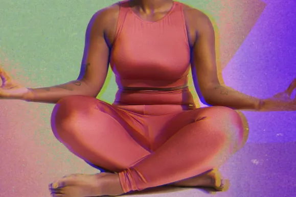 Person in coral athletic wear sitting in meditation pose against colorful purple and green gradient background