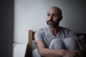 anxious man sitting alone in dimly lit room wondering what are the dangers of bulimia