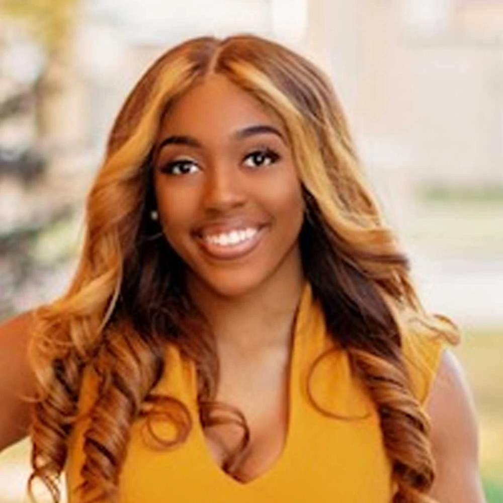 Portrait of Sheiylciea Grigsby, a smiling person with long reddish-brown hair wearing a yellow halter top