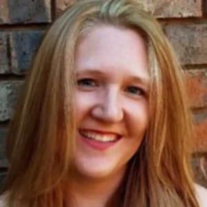 Woman with reddish-brown hair smiling at camera against brick wall background