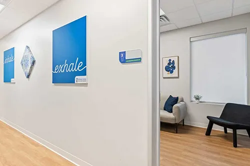 Modern wellness clinic interior with blue 'exhale' wall art, geometric patterns, and minimal furnishings in calm neutral tones