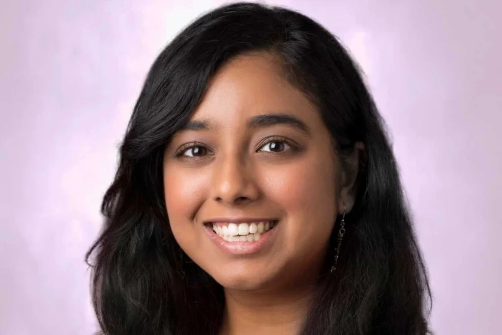 Smiling woman with long black hair against light purple background wearing earrings