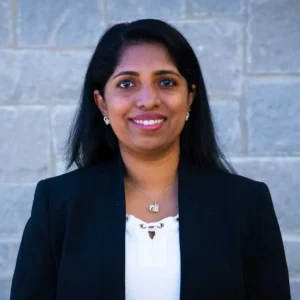 Professional portrait of a woman with long dark hair wearing a dark blazer and white top with a pendant necklace