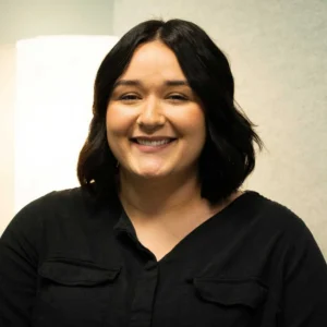 Portrait of Ellyse Garcia, a smiling person with long black hair wearing a black collared shirt indoors