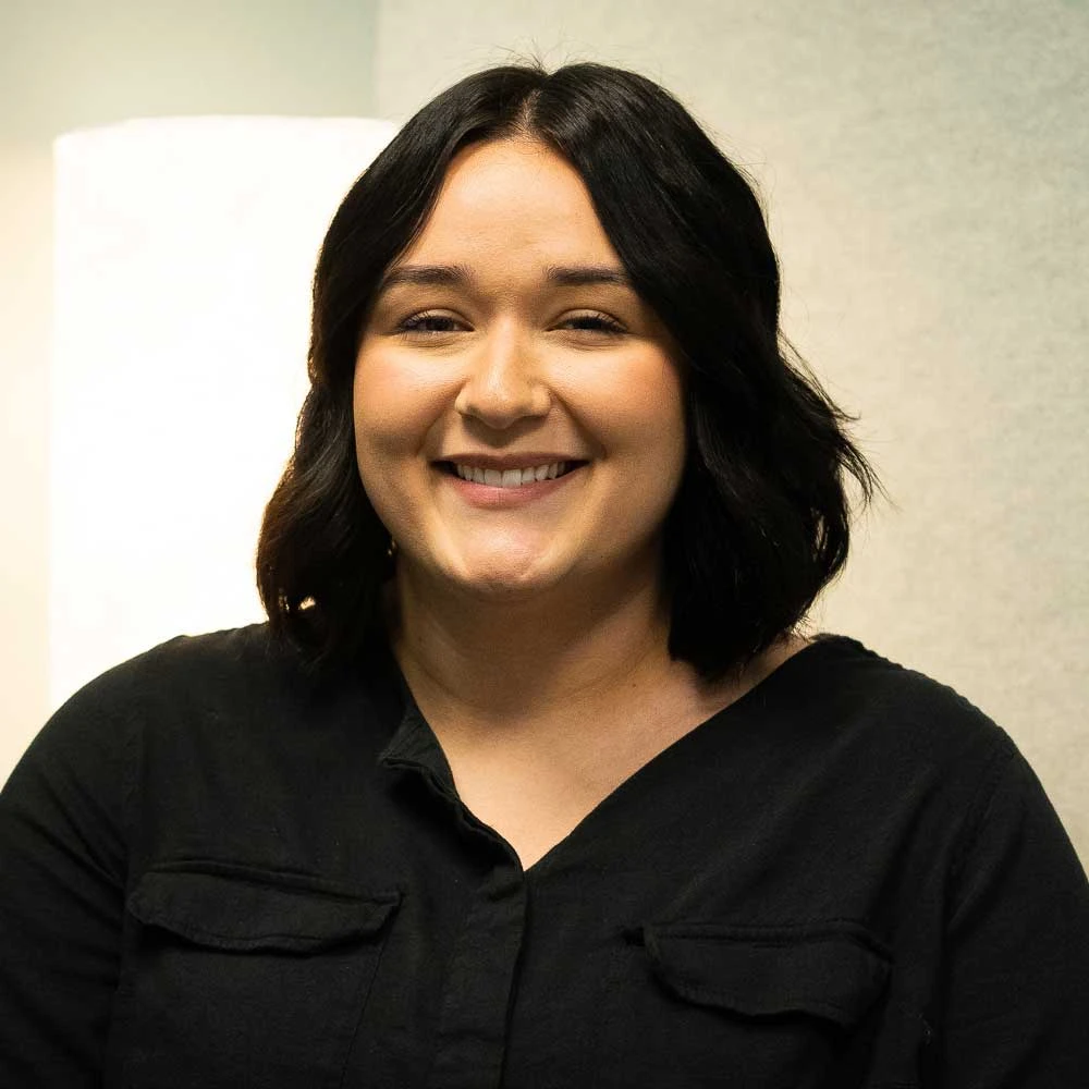 Portrait of Ellyse Garcia, a smiling person with long black hair wearing a black collared shirt indoors