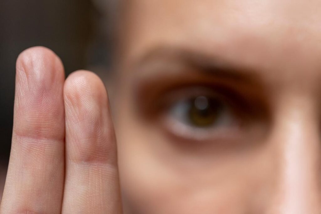 close up image of a woman's eye as she hold her fingers up in front of her face demonstrating one of the 5 benefits of EMDR therapy