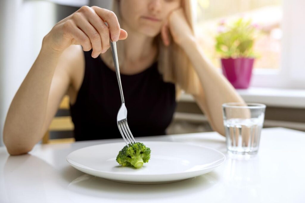 young woman with only a single piece of broccoli on her plate demonstrating one of the most common eating disorders