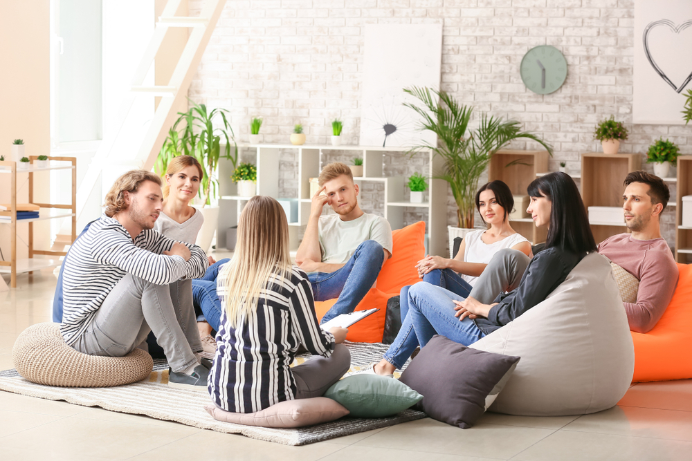 A group of individuals sitting comfortably on bean bags in a room, engaged in group therapy and conversation.