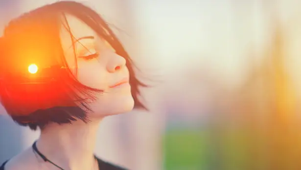 Woman with short dark hair in profile with warm golden sunlight glowing on her face against blurred background