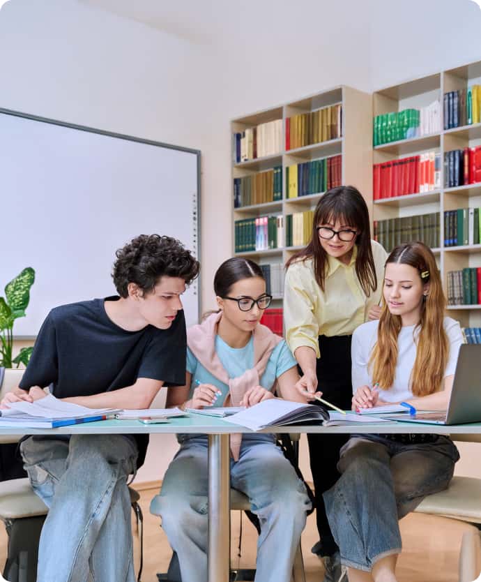 Students studying together at a table while a teacher helps guide their learning
